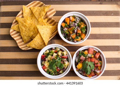Corn chips and three different salsas on a striped wooden board 