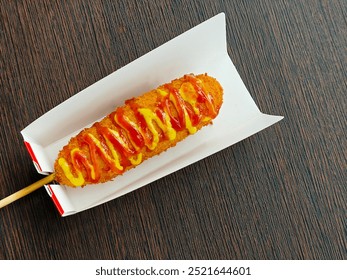 Corn dog on a paper plate, South Korean street food. Sausage and cheese wrapped in flour batter, fried and drizzled with mustard and tomato ketchup - Powered by Shutterstock