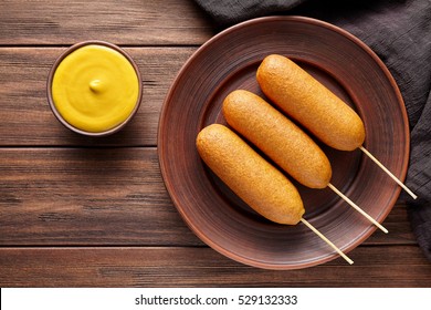 Corn Dog Traditional American Corndog Street Junk Food Deep Fried Hotdog Sausage With Mustard Snack Treat Coated In A Thick Layer Of Cornmeal Batter On Stick Unhealthy Eating On Rustic Wooden Table.