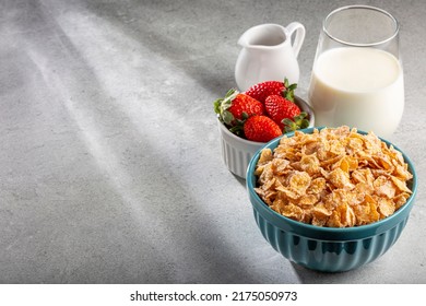 Corn flakes in the bowl with berries and milk on the table.