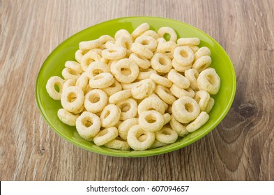 Corn flakes rings in green bowl on wooden table