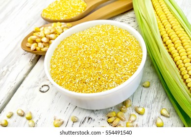 Corn grits in a bowl, cobs and kernels in a spoon on a background of wooden boards