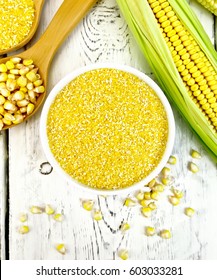 Corn grits in a bowl and spoon, cobs and grains on the background of the wooden planks on top