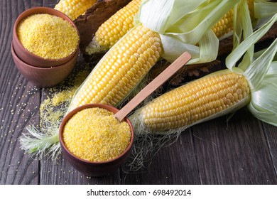 Corn grits polenta in a  ceramic bowl on white table with ripe raw corn cob and green leaves