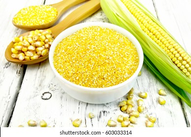 Corn grits in a white bowl and spoon, cobs and grains on the background of wooden boards