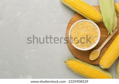 Corn groats with fresh cobs on concrete background, top view