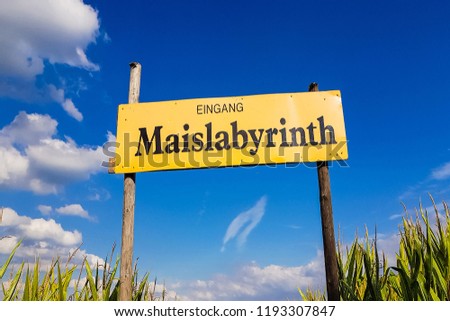 Corn Maze is a maze cut from a corn field. Maize labyrinths are popular with tourists and children. Entrance sign in front of blue sky with lettering in german - entrance Maislabyrinth
