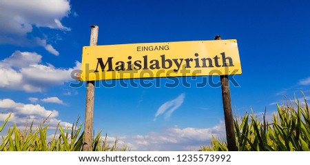 Corn Maze is a maze cut from a corn field. Maize labyrinths are popular with tourists and children. Entrance sign in front of blue sky with lettering in german - entrance Maislabyrinth