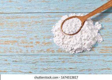 Corn starch in a wooden spoon on a wooden table, top view.