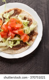 Corn Tortilla Tostada With Refried Beans, Lettuce, Salsa, And Tomatoes Top View On A Dark Wooden Background