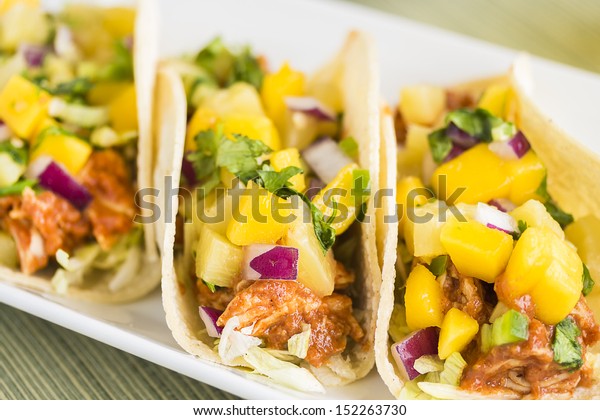 Corn tortillas\
filled with shredded lettuce, shredded barbecue chicken and topped\
with mango pineapple salsa