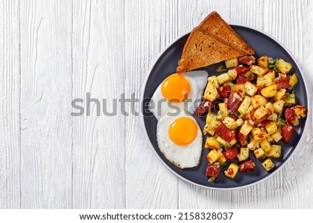 Corned Beef Hash Browns with sunny side up fried eggs and toasted rye bread on plate on white wood table, horizontal view from above, flat lay, free space