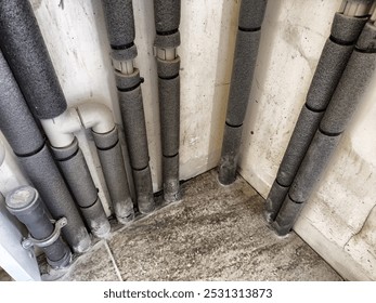 The corner of a basement features multiple insulated pipes, showcasing their arrangement and the materials used for insulation.