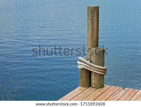 The corner of a boat dock, on a lake, with rope wrapped around pilings. 
