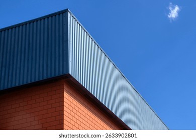 Corner of a building featuring a brick base and blue metal siding, showcasing a contrast in materials and contemporary architecture.