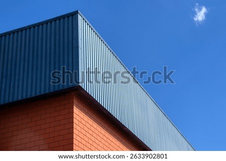 Corner of a building featuring a brick base and blue metal siding, showcasing a contrast in materials and contemporary architecture.