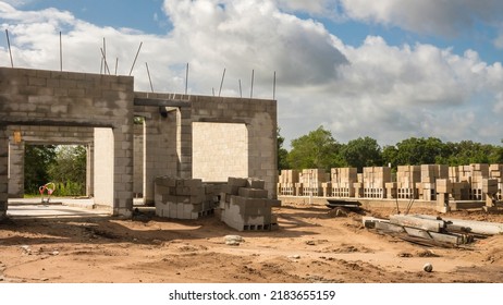 Corner Of Concrete Shell Of Single-family House Under Construction Near Stacks Of Concrete Blocks On Foundation Of Another Future House In A Suburban Development On A Sunny Morning In Florida