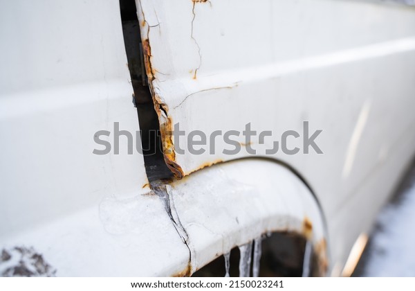 Corner of the driver\'s door of a white car with\
a dent and corrosion,\
close-up
