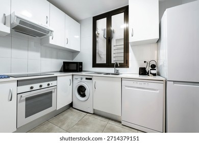 Corner of a fully fitted white kitchen with matching white appliances and ceramic tile flooring
