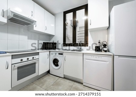 Corner of a fully fitted white kitchen with matching white appliances and ceramic tile flooring