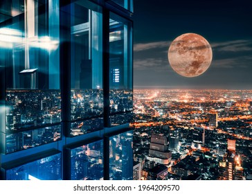 Corner Glass Window Of Skyscraper With Supermoon Glowing On Illuminated City At Bangkok