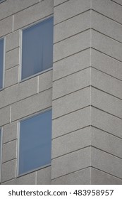 Corner of gray multi storey building with windows reflecting blue sky.
