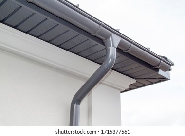 Corner of the house with new gray metal tile roof and rain gutter. Metallic Guttering System, Guttering and Drainage Pipe Exterior