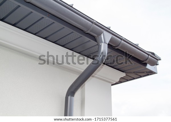 Corner of the house with new gray metal tile
roof and rain gutter. Metallic Guttering System, Guttering and
Drainage Pipe Exterior