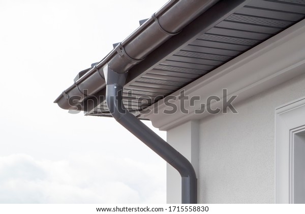 Corner of the house with new gray metal tile\
roof and rain gutter. Metallic Guttering System, Guttering and\
Drainage Pipe Exterior