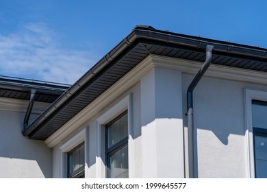 Corner of house with windows, new gray metal tile roof and rain gutter. Metallic Guttering System, Guttering and Drainage Pipe Exterior