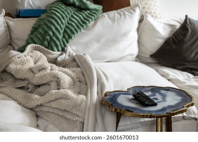 Corner of a Large White Sofa Couch with Throw Pillows blankets and a cute table with TV remotes