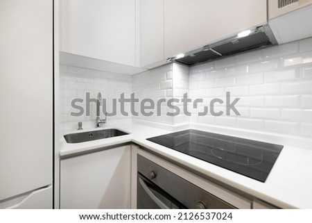 Corner of a modern kitchen with ceramic hob, extractor hood, stainless steel oven, sink embedded in the stone composite countertop