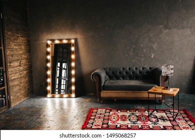 Corner room with a wooden and  gray cement wall, an aged floor, black glass doors and electric dressing makeup mirror, lights bulbs tern on, sofa. Loft style - Shutterstock ID 1495068257