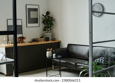 Corner of spacious hi-tech office with comfortable black leather couch standing in front of small round decorative table with flowerpot - Shutterstock ID 2380066211