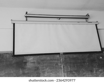 In the corner of the vintage classroom, an elegant projector screen unfurls its canvas of memories. Aged but proud, it bears the marks of countless lessons. - Shutterstock ID 2364293977