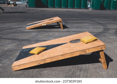 Cornhole game set, process of throwing bean bags, kids children tossing bean sacks, corn hole  in the backyard, wooden boards for corn-hole tournament in the summer sunny day