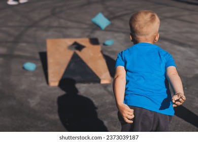 Cornhole game set, process of throwing bean bags, kids children tossing bean sacks, corn hole  in the backyard, wooden boards for corn-hole tournament in the summer sunny day