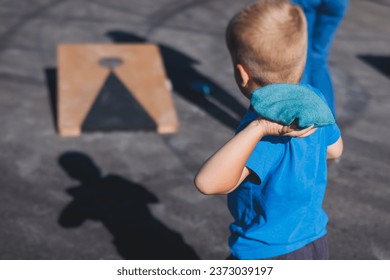 Cornhole game set, process of throwing bean bags, kids children tossing bean sacks, corn hole  in the backyard, wooden boards for corn-hole tournament in the summer sunny day