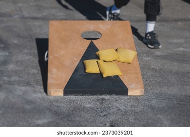 Cornhole game set, process of throwing bean bags, kids children tossing bean sacks, corn hole  in the backyard, wooden boards for corn-hole tournament in the summer sunny day