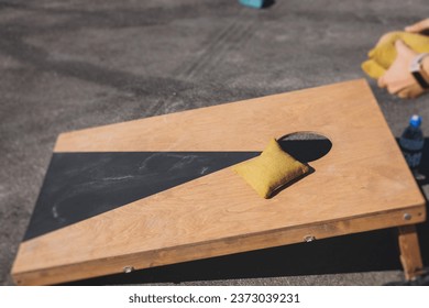Cornhole game set, process of throwing bean bags, kids children tossing bean sacks, corn hole  in the backyard, wooden boards for corn-hole tournament in the summer sunny day