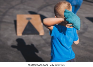 Cornhole game set, process of throwing bean bags, kids children tossing bean sacks, corn hole  in the backyard, wooden boards for corn-hole tournament in the summer sunny day