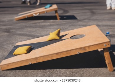 Cornhole game set, process of throwing bean bags, kids children tossing bean sacks, corn hole  in the backyard, wooden boards for corn-hole tournament in the summer sunny day