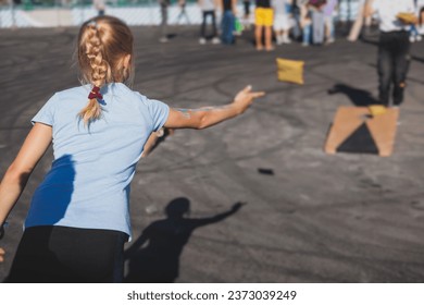 Cornhole game set, process of throwing bean bags, kids children tossing bean sacks, corn hole  in the backyard, wooden boards for corn-hole tournament in the summer sunny day