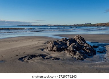 Cornish beach with rocks and far distant view of Porthscatho.