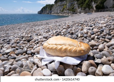 Cornish pasty on shingle beach with sea in background - Shutterstock ID 1420614740