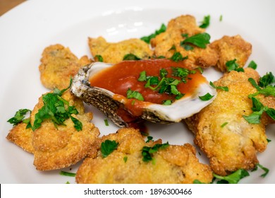 Cornmeal Fried Oysters In A White Bowl With Cocktail Sauce Inside Of An Oyster Shell. The Dish Is Topped With Chopped Parsley.