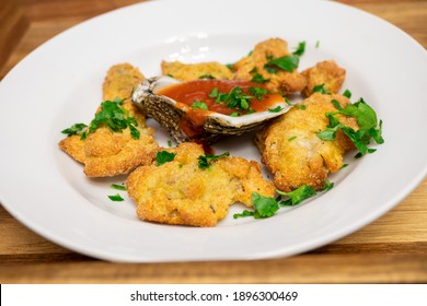 Cornmeal Fried Oysters In A White Bowl With Cocktail Sauce Inside Of An Oyster Shell. The Dish Is Topped With Chopped Parsley.