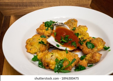 Cornmeal Fried Oysters In A White Bowl With Cocktail Sauce Inside Of An Oyster Shell. The Dish Is Topped With Chopped Parsley.