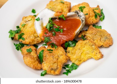 Cornmeal Fried Oysters In A White Bowl With Cocktail Sauce Inside Of An Oyster Shell. The Dish Is Topped With Chopped Parsley.