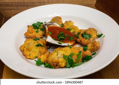 Cornmeal Fried Oysters In A White Bowl With Cocktail Sauce Inside Of An Oyster Shell. The Dish Is Topped With Chopped Parsley.